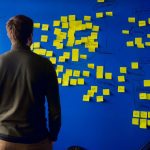 Bootstrapping vs. Fundraising Choosing the Right Path for Your Startup Person standing in front of a wall filled with sticky notes and trying to decide between bootstrappi